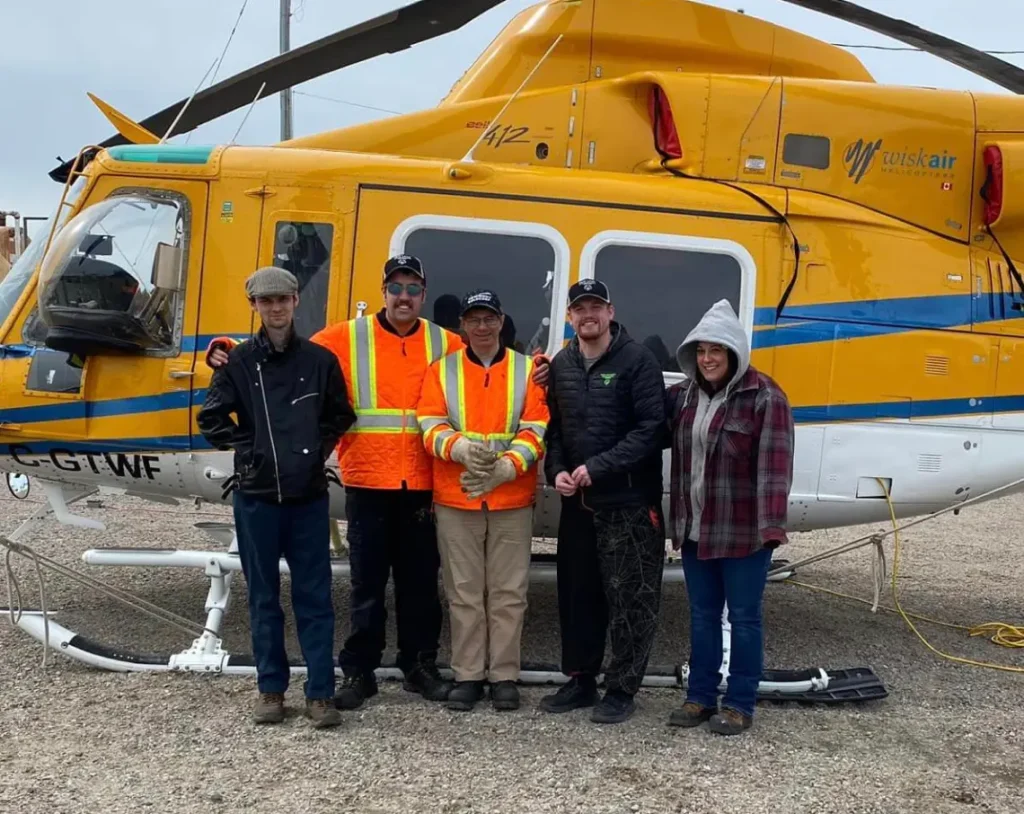 Harmony Centre participants and staff posing in front of a Wisk Air helicopter at a remote work site during a supported employment program outing.