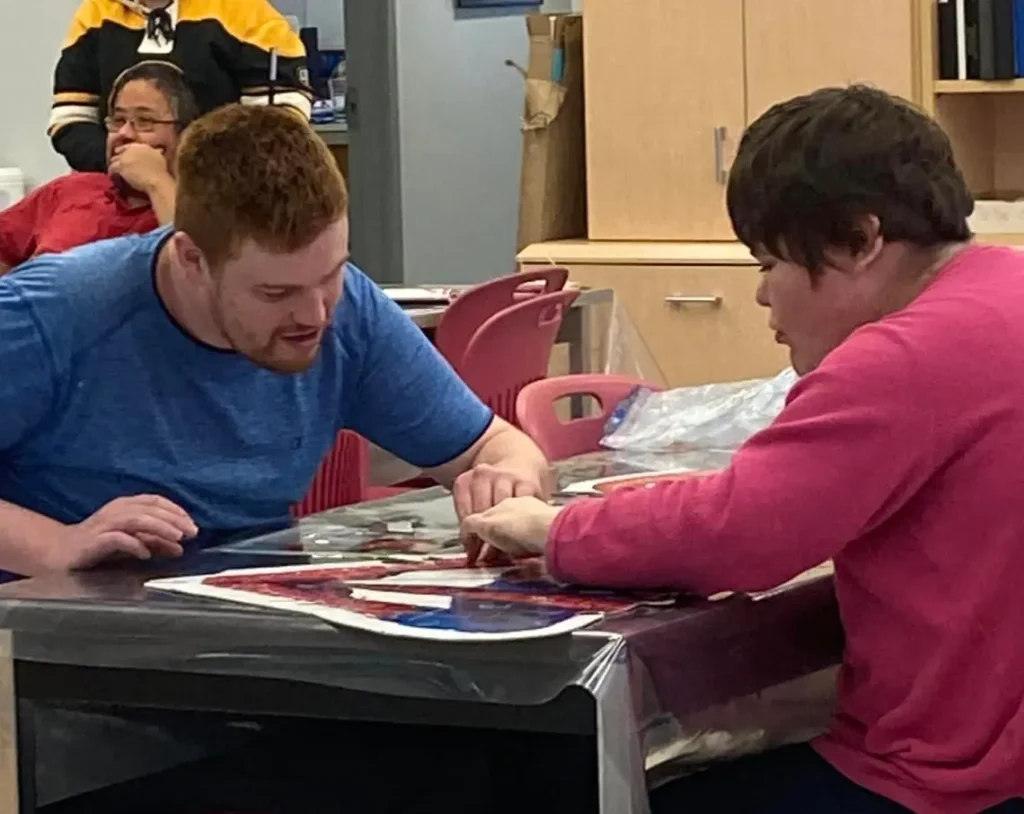 Harmony Centre staff member working one-on-one with a participant on a puzzle activity at a program table.
