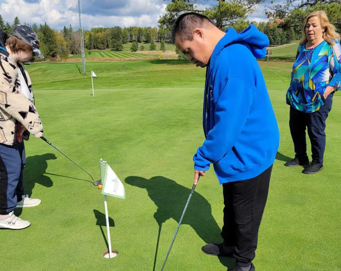 Harmony Centre participant putting on a golf green during an outdoor recreation outing, supported by staff.