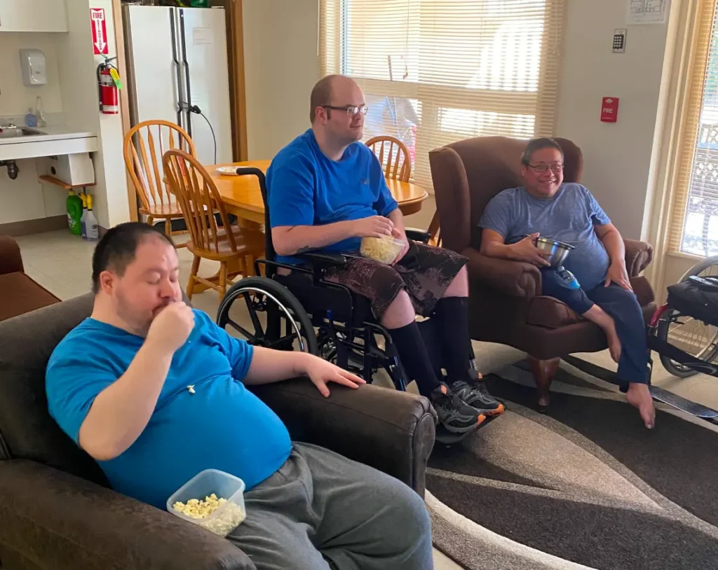 Three Harmony Centre participants relaxing together in a comfortable living room, enjoying popcorn and a movie.